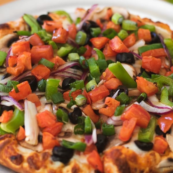 Close-up of a Red Tomato Pizza House pizza, topped with diced tomatoes, green peppers, olives, and onions.