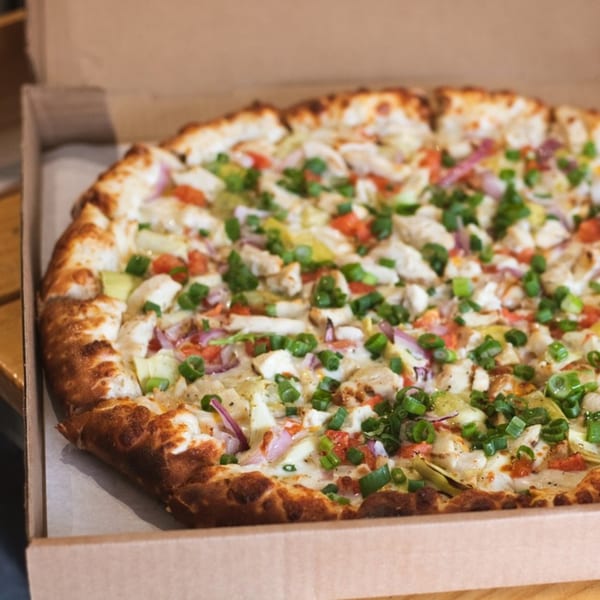 Red Tomato Pizza House's chicken pizza with red onions, tomatoes, and green onions in a box.