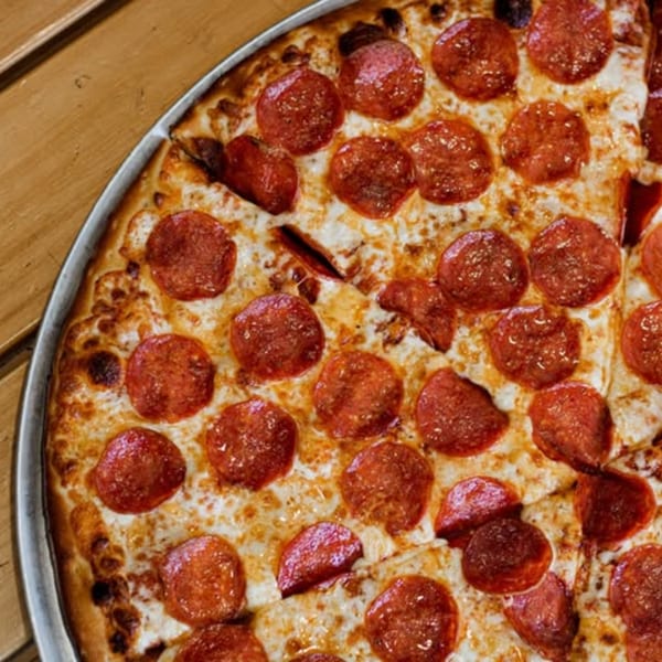 Close-up of a Red Tomato Pizza House pepperoni pizza with melted cheese on a wooden table.